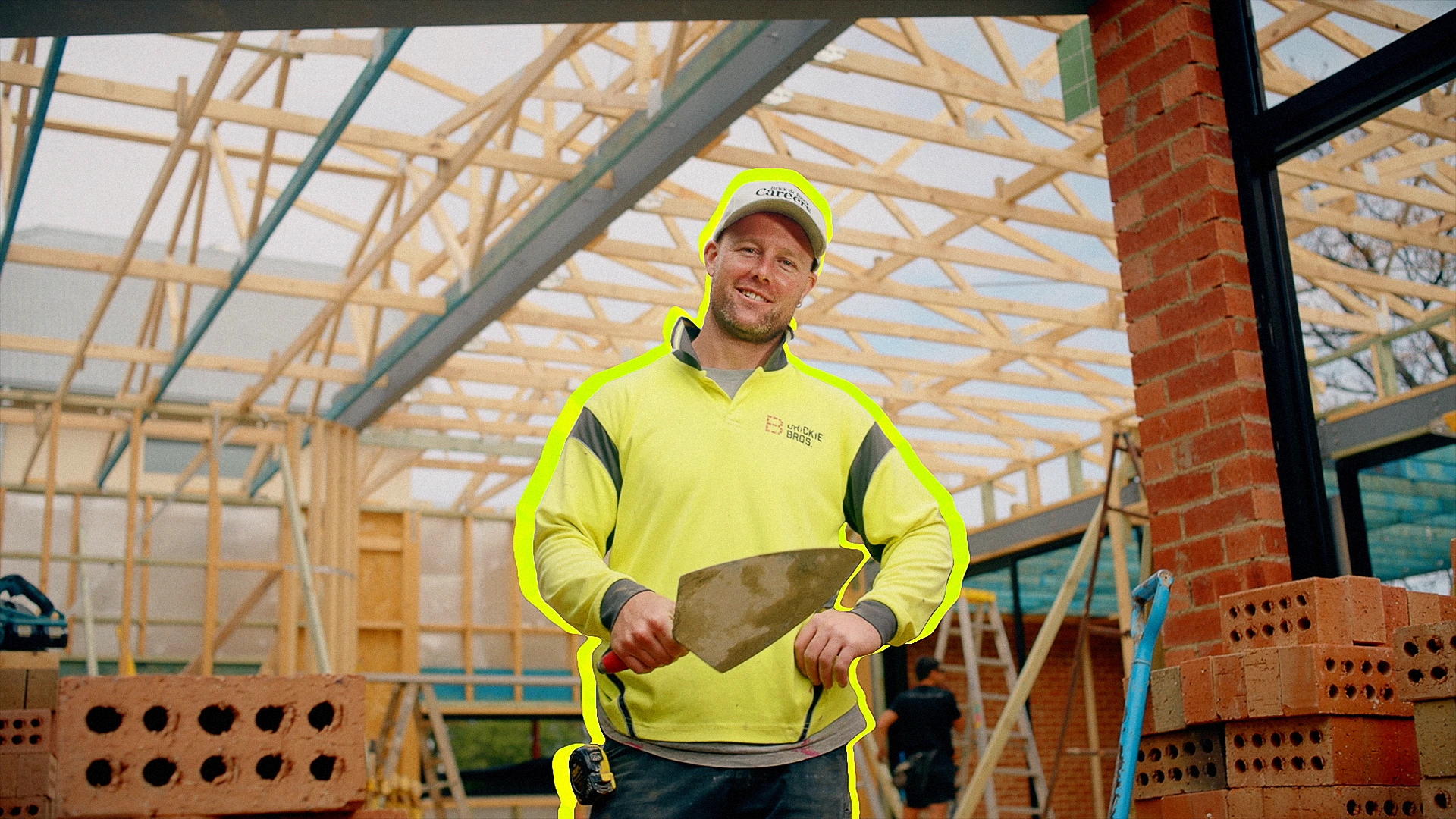 Kyle the Labourer, wearing hi vis in a construction site, holding a trowel